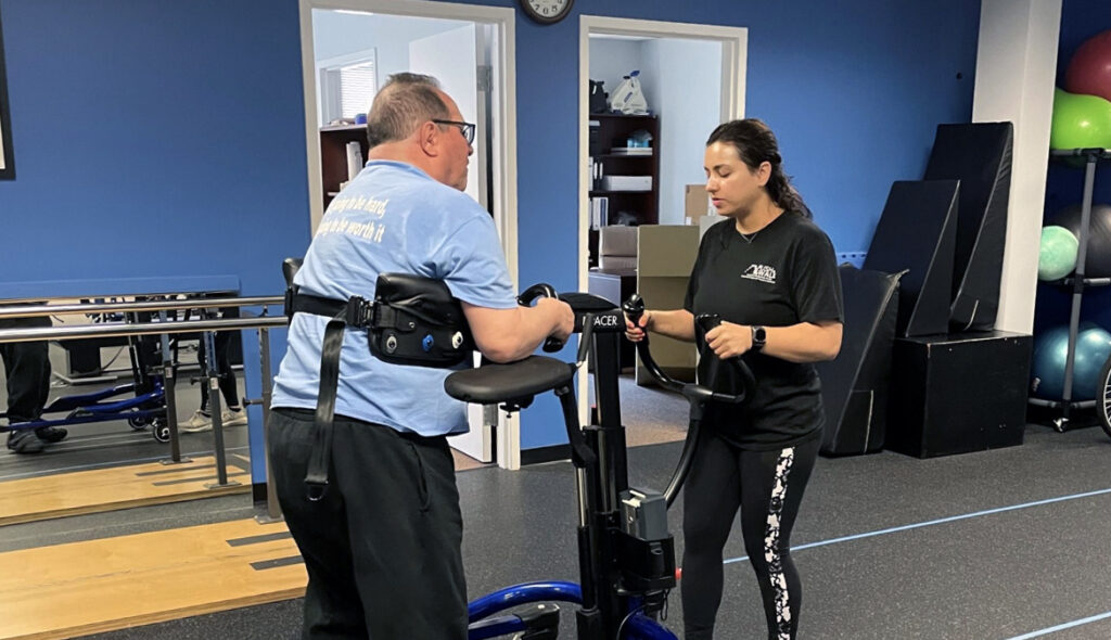 A Push to Walk trainer works with a client using equipment to walk across the gym floor