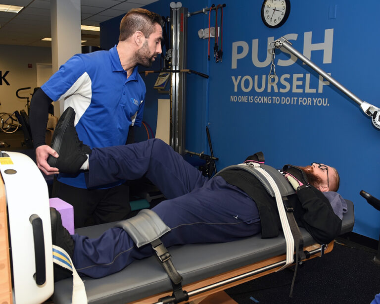 A trainer works with a client laying on a table in the Push to Walk gym to increase mobility.