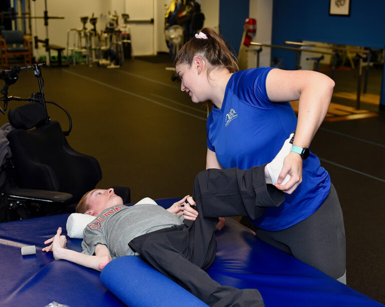 A trainer works with a Push to Walk client's legs in the gym