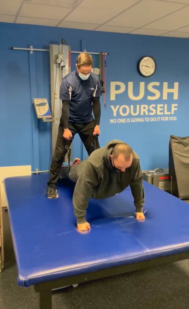A trainer helps a client exercise on a mat at the Push to Walk gym