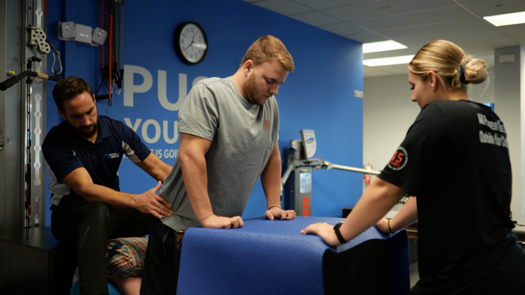 Two trainers work with a client at the Push to Walk gym.